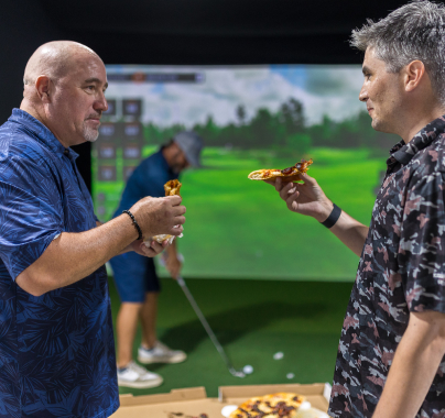 2 men eating pizza and chatting at Fairway Golf simulator facility in San Antonio