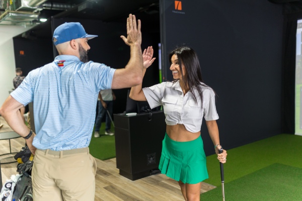 A man and woman practice their swings in a golf simulator during an indoor lesson in San Antonio.