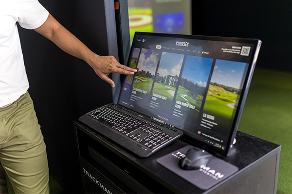 A man points at a computer screen displaying a golf course, promoting Trackman as a tool for improving swing performance.