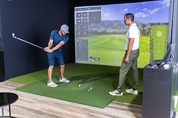 Two men enjoying a round of golf on a simulator in a modern training room, showcasing technology in sports.