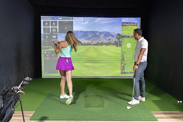 Two golfers using a simulator in a room, highlighting the benefits of indoor practice during the fall season. Fairway San Antonio
