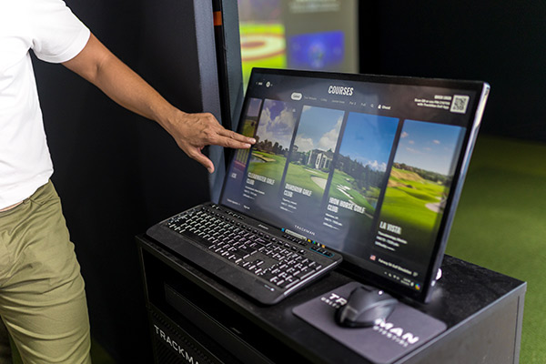 Trackman: A man gestures towards a computer screen showing a golf game, illustrating why indoor simulators are ideal for fall training.