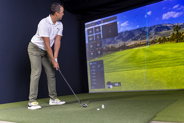 Inside a room, a man engages with a golf simulator, highlighting expert advice on Texas golf courses.