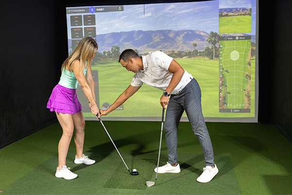 A man and woman engaged in a golf simulator session, learning advanced techniques to enhance their game.