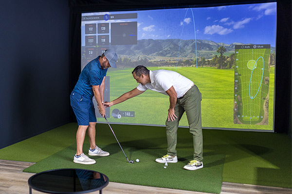 Two men engaged in a golf simulator session, focusing on advanced techniques in a modern indoor setting.