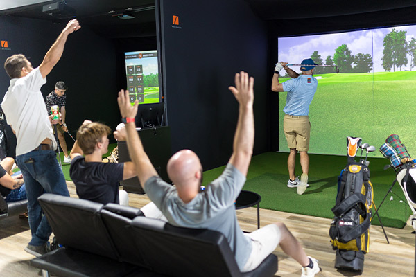 Group of individuals playing virtual golf in a cozy room, featuring a TV screen showing the golf course.