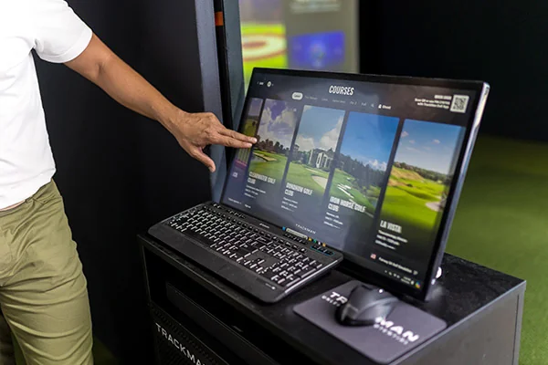 A man gestures towards a computer screen featuring HD golf simulators, highlighting ways to enhance your game this holiday.