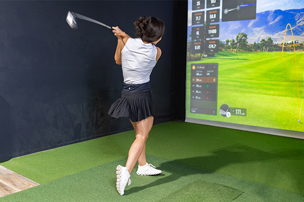  A woman is shown striking a golf ball on a video screen, demonstrating methods for effective indoor golf practice.