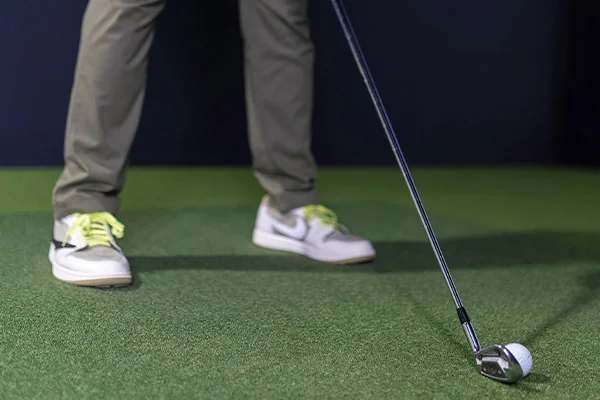 A person holds a golf club on a green, demonstrating techniques for effective indoor golf practice.