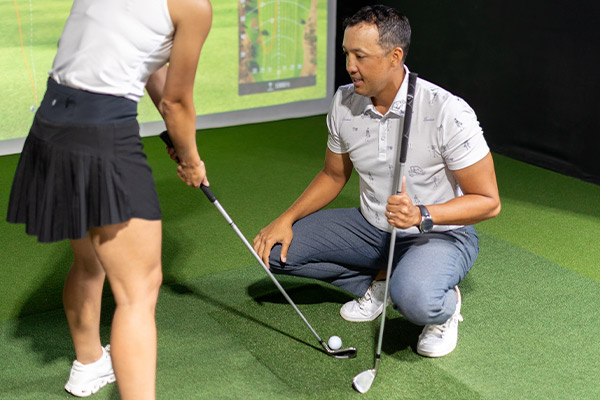 A man and woman engage in golf practice using a simulator, highlighting affordable lessons available in San Antonio.