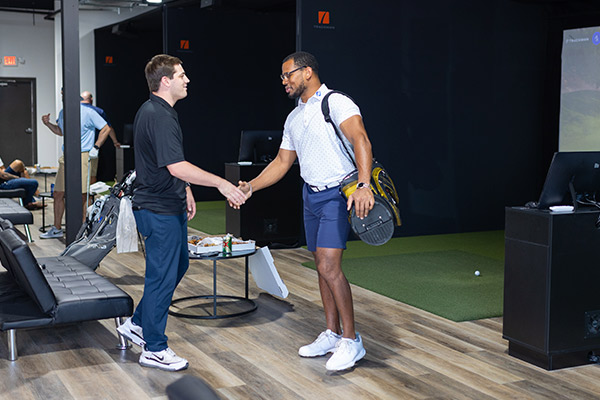 two men in a golf room shaking hands, representing affordable golf lesson options in San Antonio.