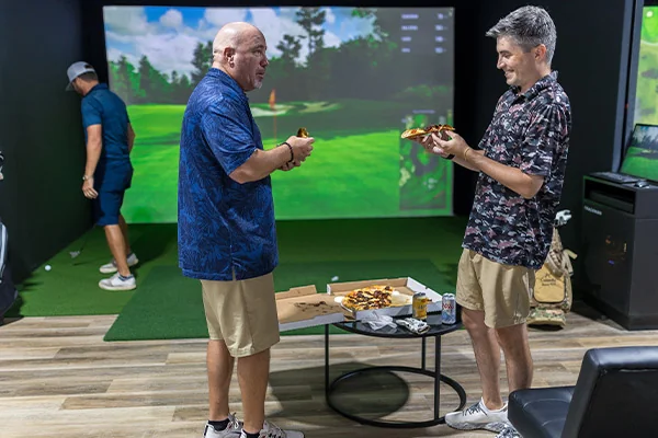 Two men enjoying a round of golf in a golf simulator room during a corporate event in San Antonio.