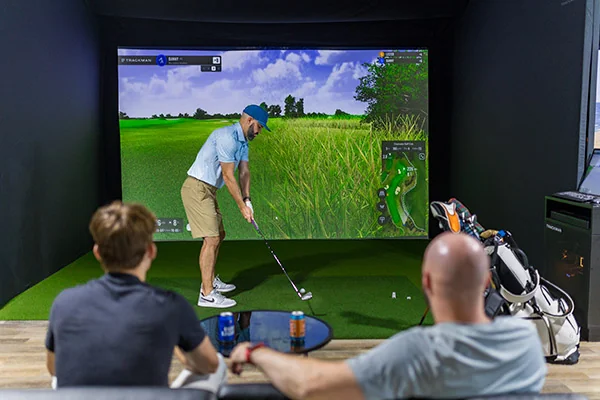A man engages with a golf simulator in a room designed for corporate events in San Antonio, highlighting interactive entertainment.