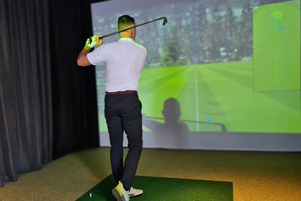 A man engages with a golf simulator, analyzing his swing in a room designed for data-driven performance improvement.