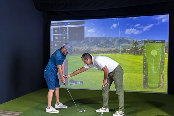 Two men engage in a golf simulator session, utilizing analysis data to enhance their swing techniques and skills.