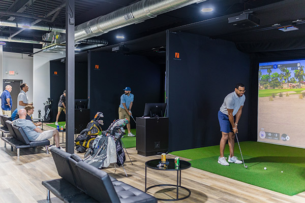 People engaged in a golf simulator room, focusing on swing analysis and data-driven techniques for improvement.