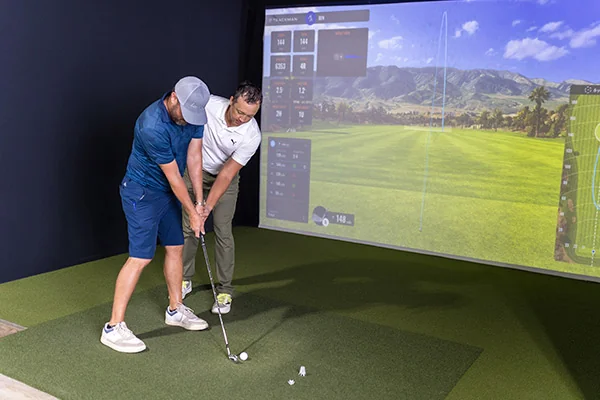 Two men engaged in a golf simulator game indoors, assessing the accuracy of their simulated scores versus real golf.