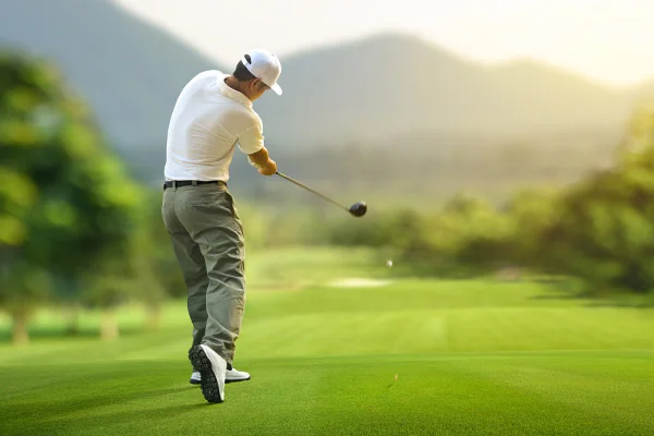 A golfer in mid-swing on a lush green field, with mountains behind, highlighting the accuracy of golf simulators versus real play.