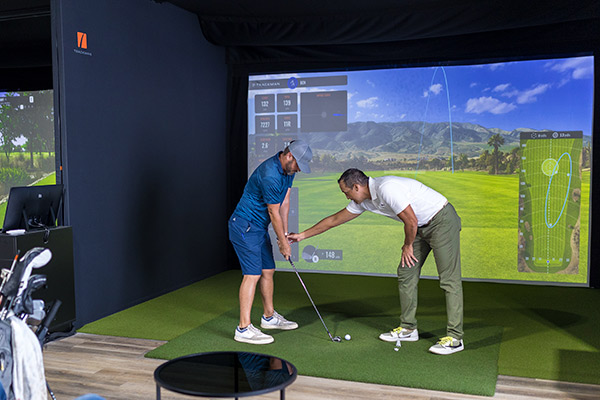 Two men engaged in a golf simulator session indoors, illustrating a fun introduction to golf lessons.