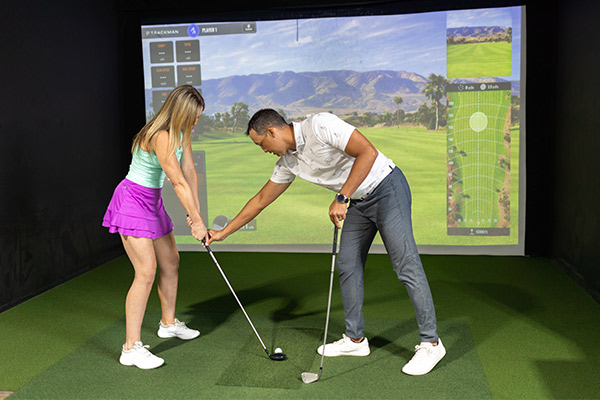 A man and woman engaged in a golf simulator session, practicing their swings during a lesson.