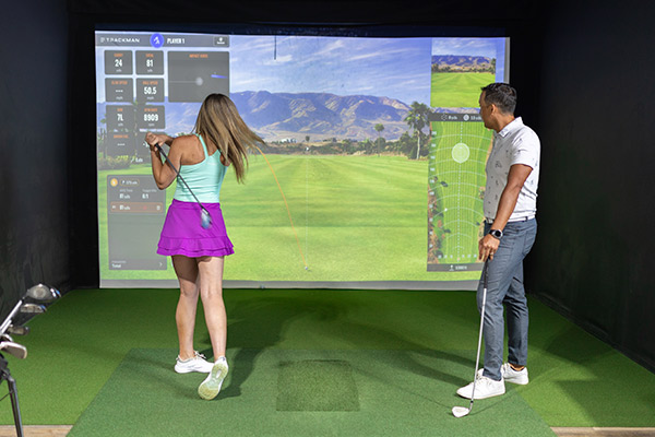 A man and woman engaged in a golf simulator session, practicing their swings as part of a first golf lesson.