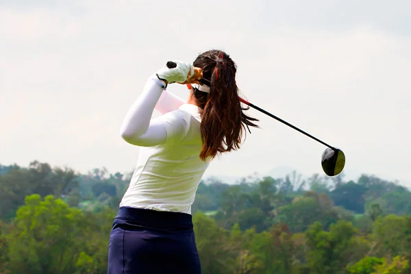 A woman in mid-swing with a golf club on a lush green field, highlighting women's growth in golf in San Antonio.