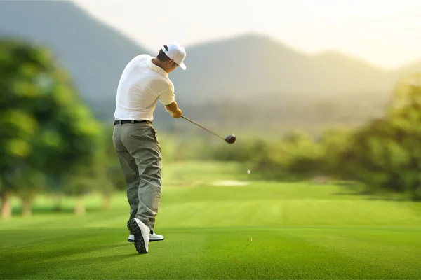 Golfer hitting golf ball with driver to fairway.