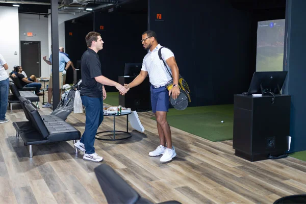  Two men shaking hands in a room featuring a golf simulator in the background