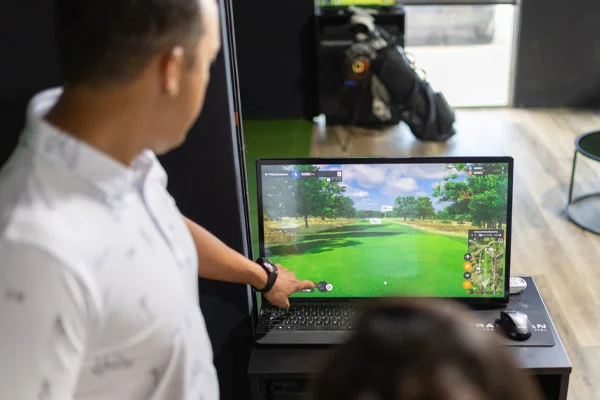 A man and woman engaged in a virtual golf game on a computer, utilizing Trackman for performance tracking.