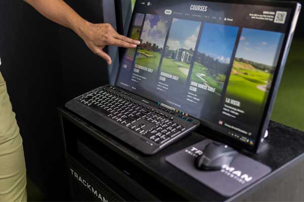 A man gestures towards a computer screen featuring a golf game, indicating his focus on the digital gameplay.
