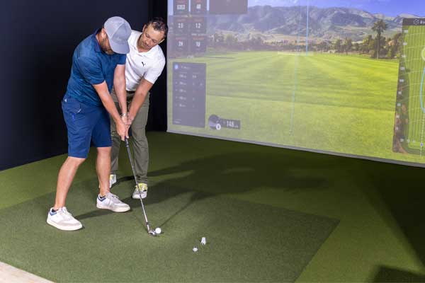 Two men playing golf on a simulator, concentrating on their shots in a well-lit indoor setting.