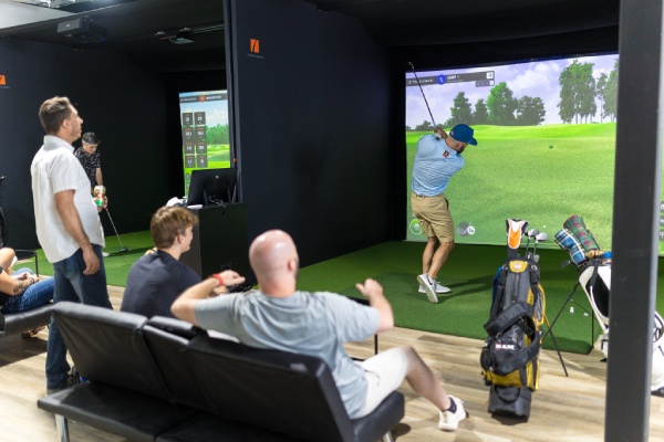 A group of people enjoying a golf simulator in a well-lit room, focused on their swings and the virtual course display.