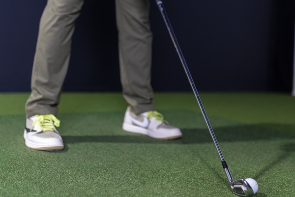 Individual standing on a putting green, focusing on their golf stroke in an indoor setting.