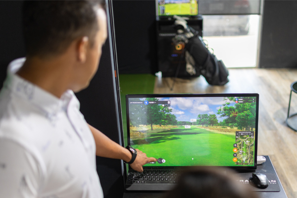 A man swings a golf club while checking trackman screen.