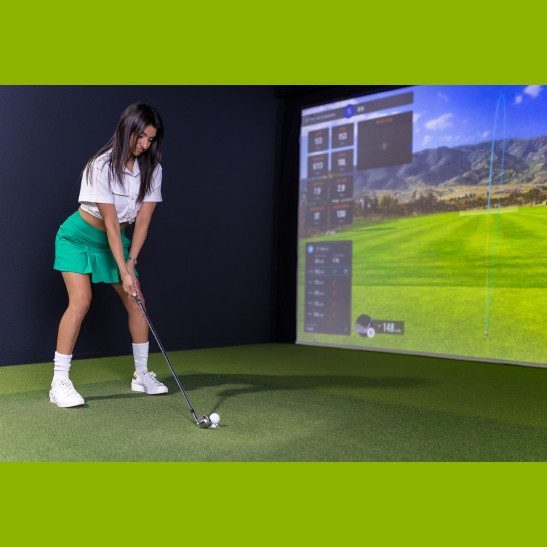 A woman in a white top and green skirt prepares to hit a golf ball in a virtual golf simulator setting.
