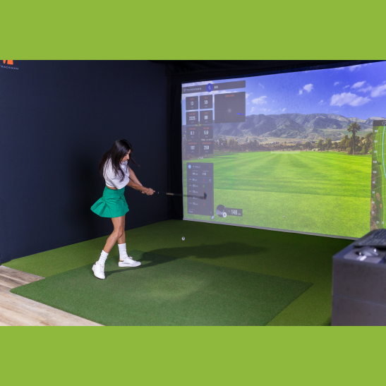 A golfer swings a club in a virtual golf simulator, with a scenic landscape displayed on the screen.