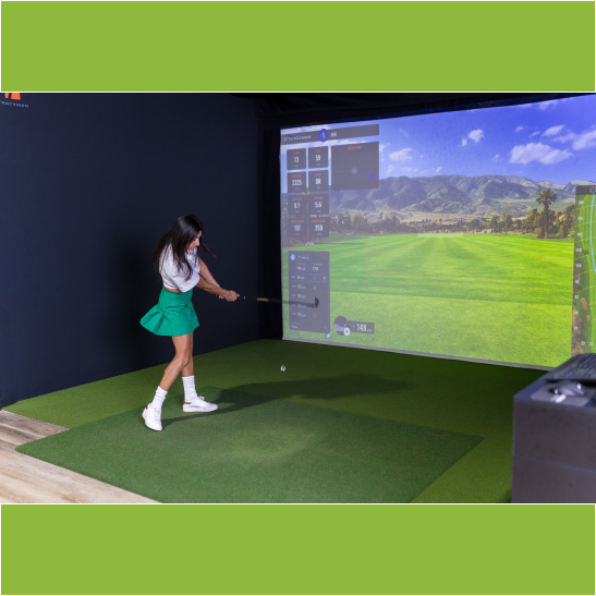 A golfer swings a club in a virtual golf simulator, with a scenic landscape displayed on the screen.