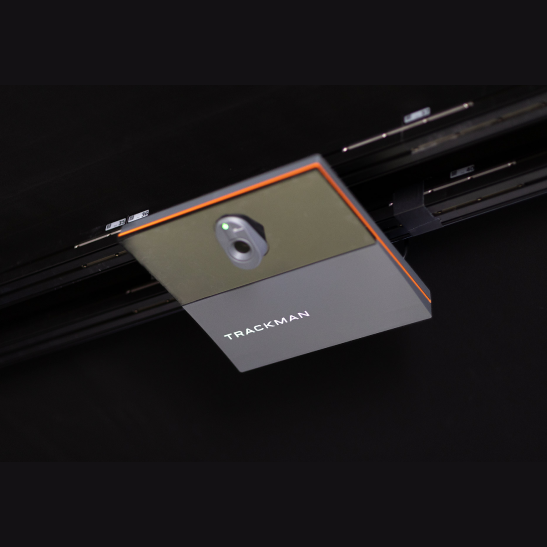 A TrackMan device mounted on a rail, featuring a lens and a green indicator light.