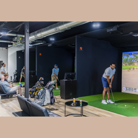 Golf enthusiasts practice their swings in a modern indoor facility with simulators, while others relax nearby.